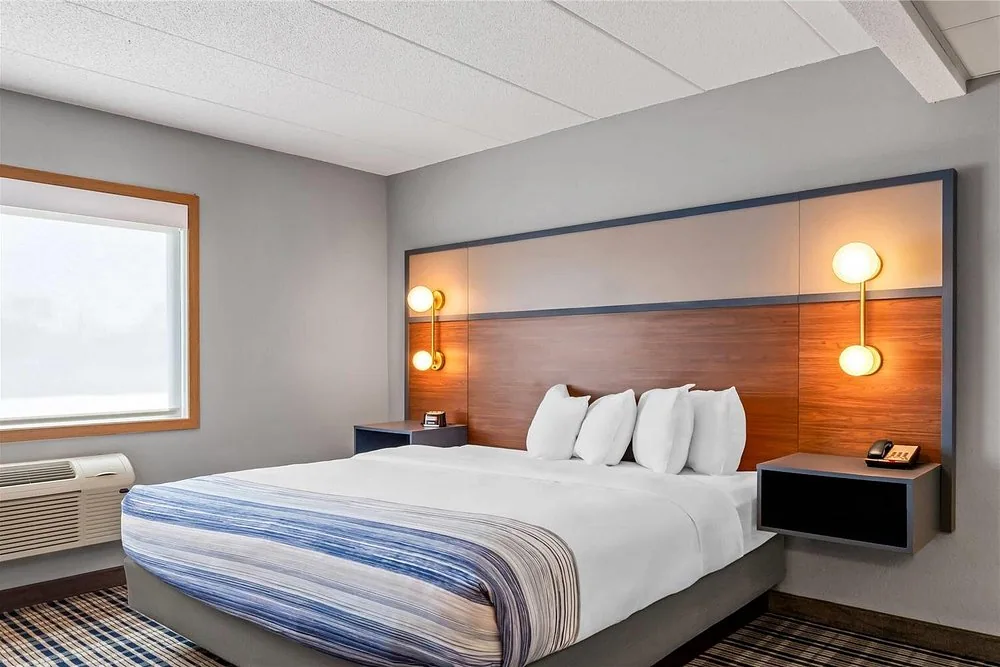 AmericInn by Wyndham Crookston — king bed with wood headboard, sconces and floating nightstands