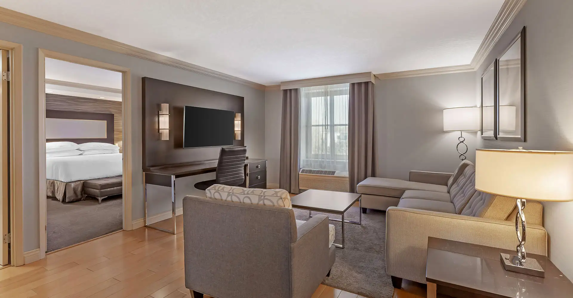 Best Western Plus The Arden Park Hotel — king deluxe suite living area with sectional sofa, accent chairs and TV console, bedroom beyond