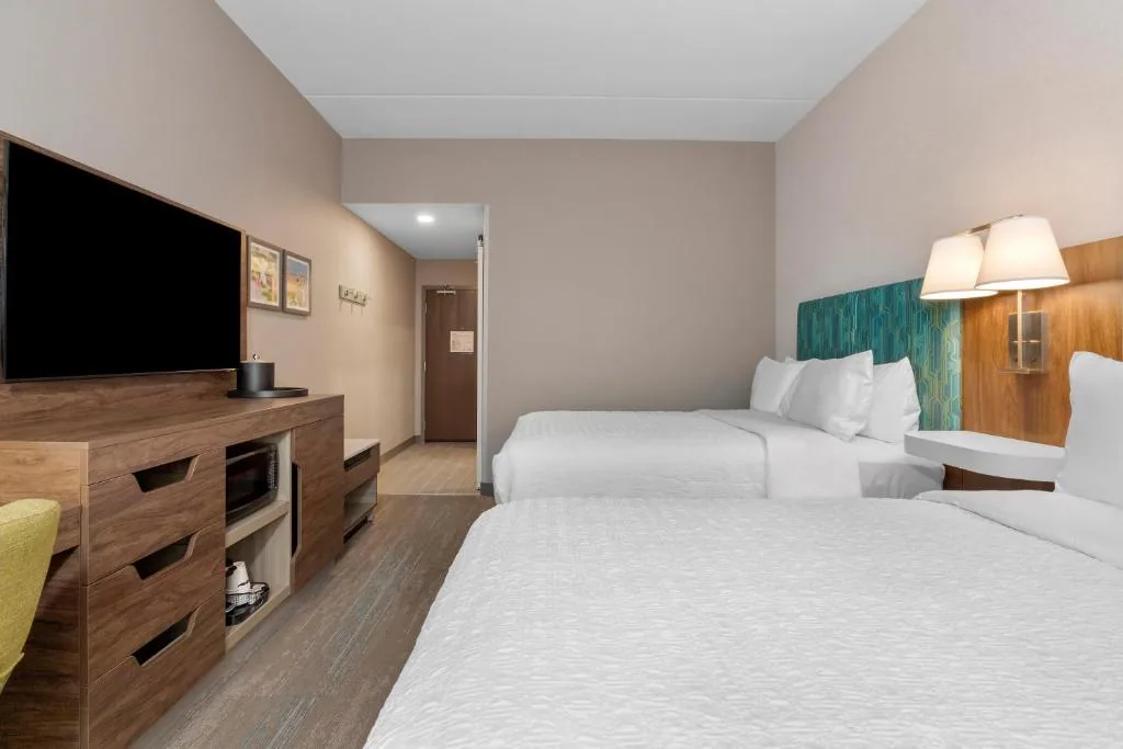 Hampton Inn & Suites Cornwall — double-queen guestroom with case goods and TV console